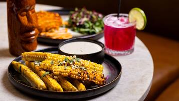 A plate of grilled corn with a dipping sauce, a salad, and a beverage with a lime garnish.