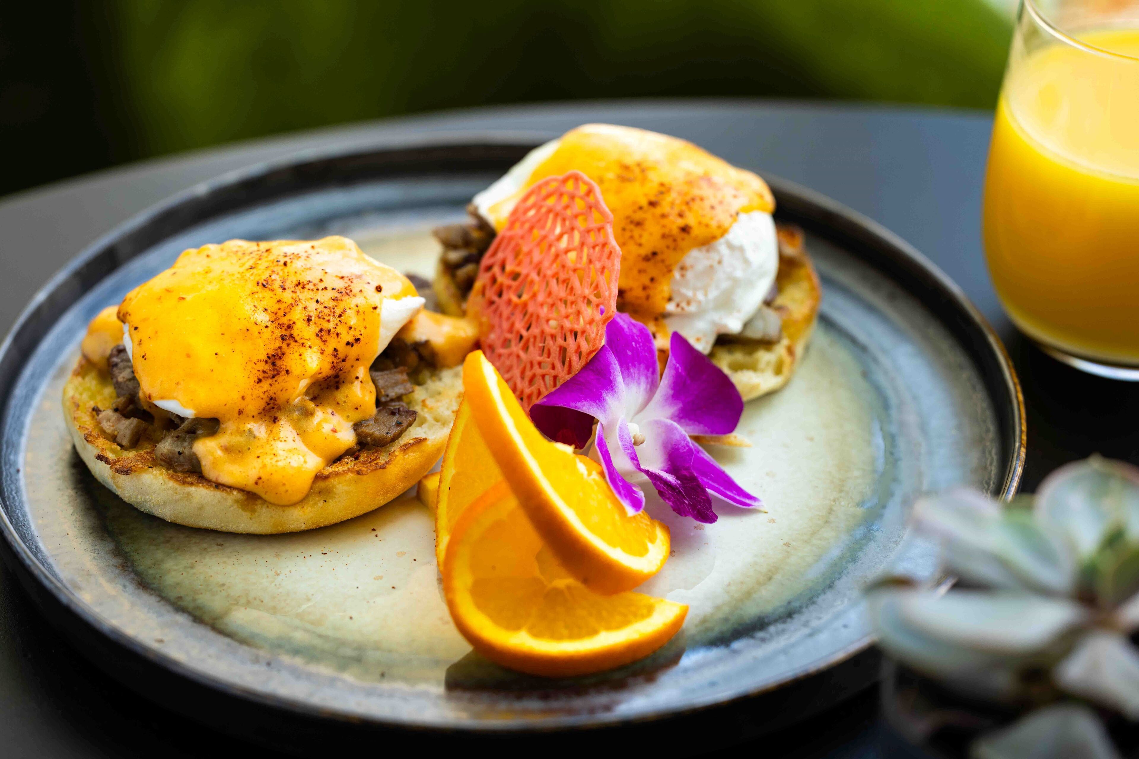 A breakfast plate with eggs, orange slices, and a flower on a ceramic plate.