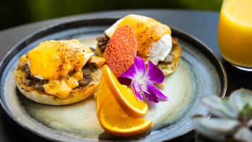 A breakfast plate with eggs, orange slices, and a flower on a ceramic plate.