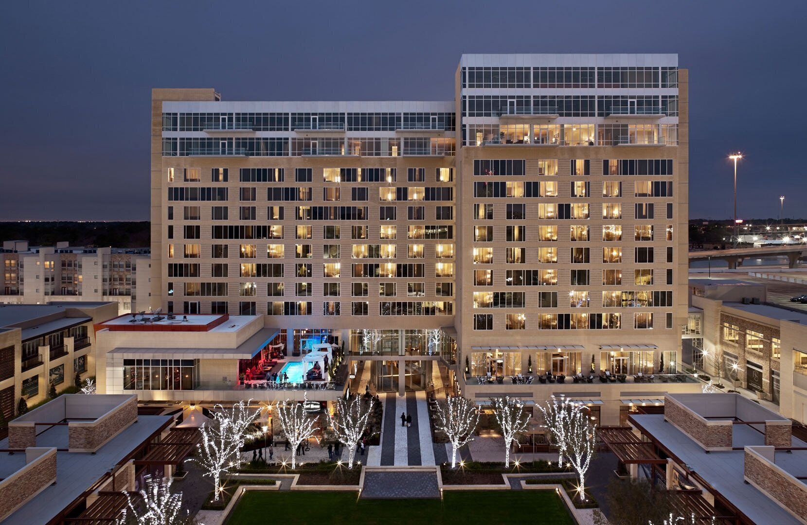 A multi-story hotel with a central courtyard, outdoor seating, and a pool area.