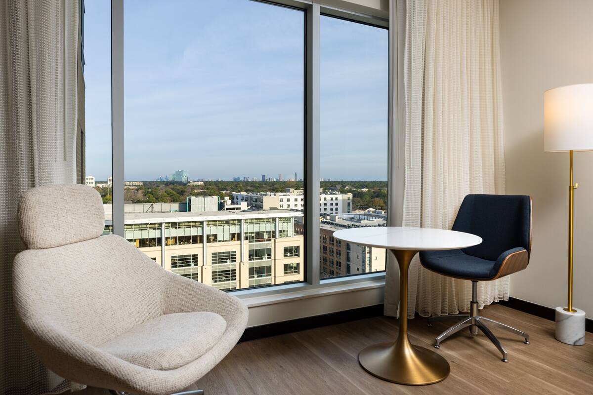 Ein modernes Zimmer mit einem großen Fenster, einem runden Tisch, einem blauen Stuhl und einem weißen Stuhl.