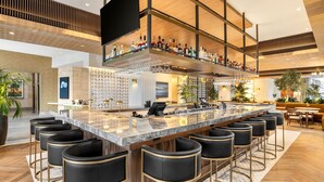 A modern bar area with a marble countertop, multiple bar stools, and a variety of bottles and glasses on shelves. - The Moran CITYCENTRE (Houston)