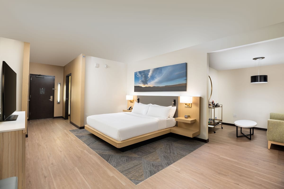 Ein modernes Hotelzimmer mit einem großen Bett, Nachttischen, einem Schreibtisch, einem Stuhl und einem Bild an der Wand.