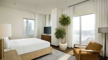 A modern hotel room with a large bed, a TV, a potted plant, a chair, and a city view.