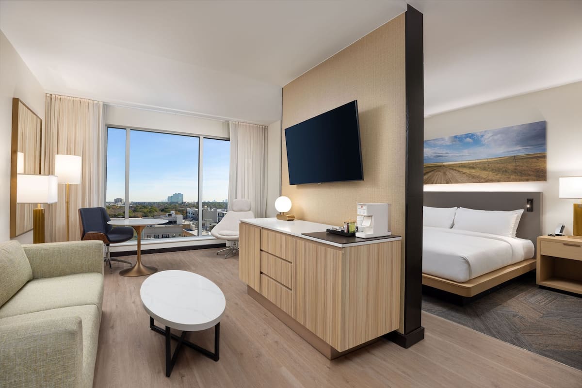 Ein modernes Hotelzimmer mit einem großen Bett, einem Schreibtisch, einer Couch und Blick auf die Stadt.