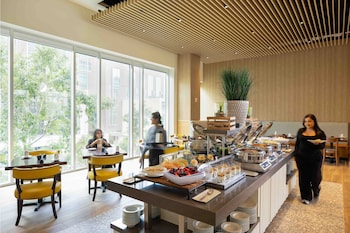 An outdoor dining area with tables and chairs, surrounded by greenery and a building with a