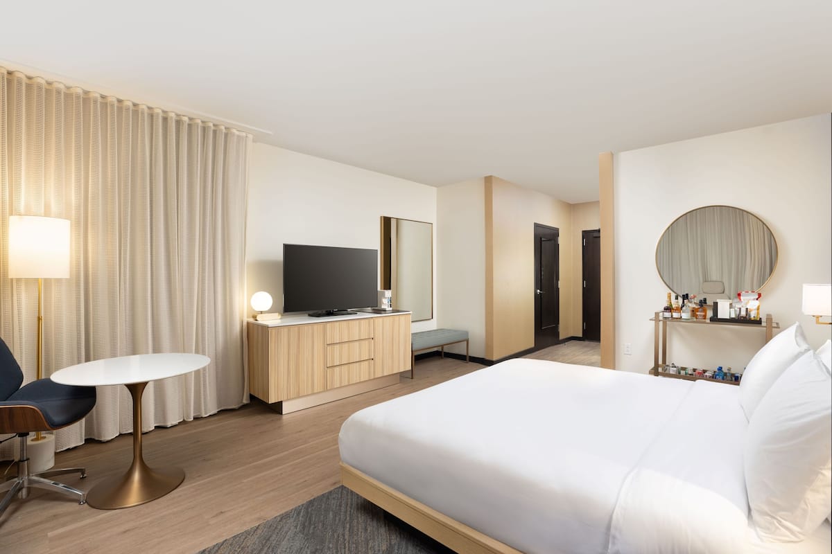 Ein Hotelzimmer mit Bett, Schreibtisch mit Fernseher, Stuhl, Nachttisch, Lampe und Spiegel.