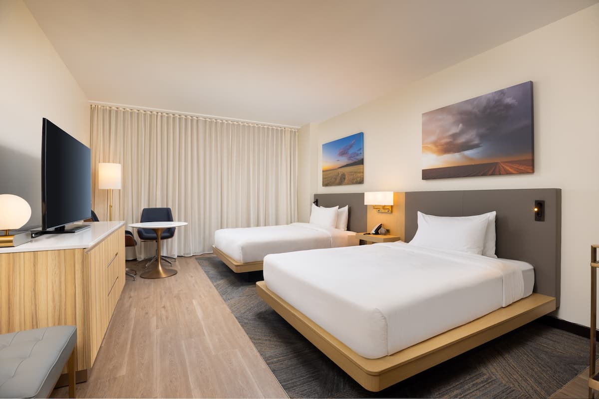 Ein Hotelzimmer mit zwei Betten, einem Schreibtisch, einem Sessel, einem Fernseher und Bildern an der Wand.