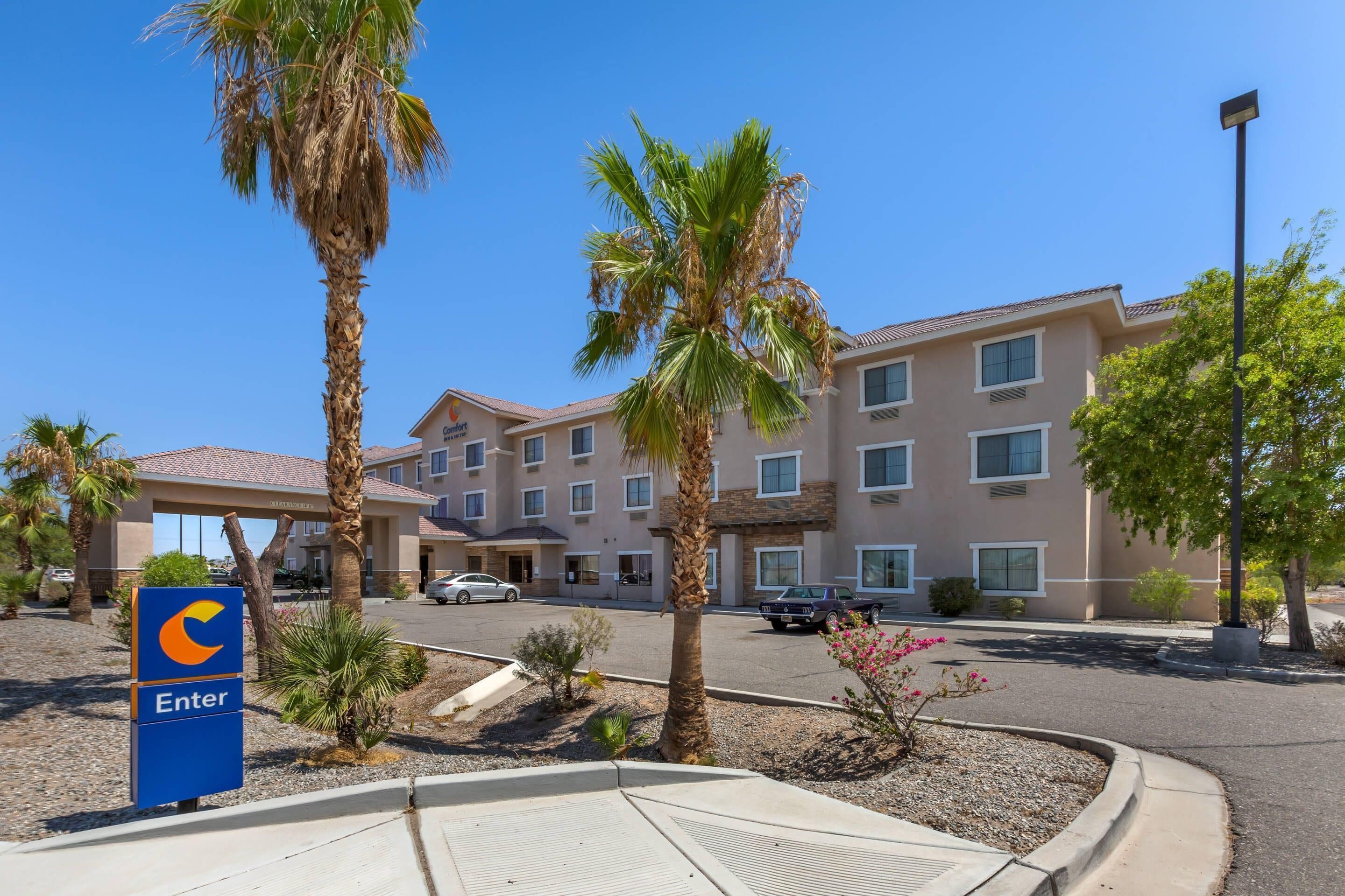 A hotel with a 'C' logo entrance sign, palm trees, and a parking lot.