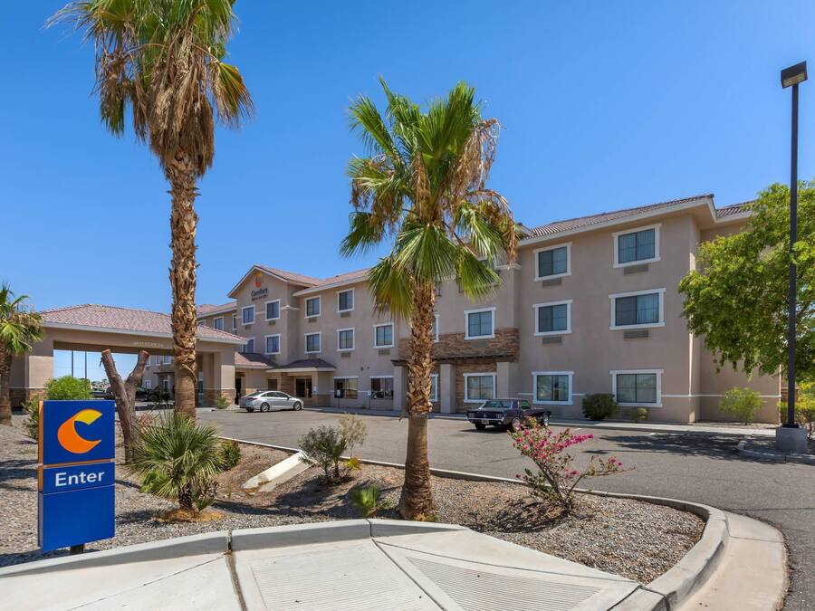 A hotel with a 'C' logo entrance sign, palm trees, and a parking lot.