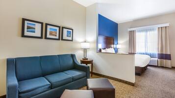 A hotel room with a blue sofa, a small table with a lamp, a bed, and framed pictures on the wall.