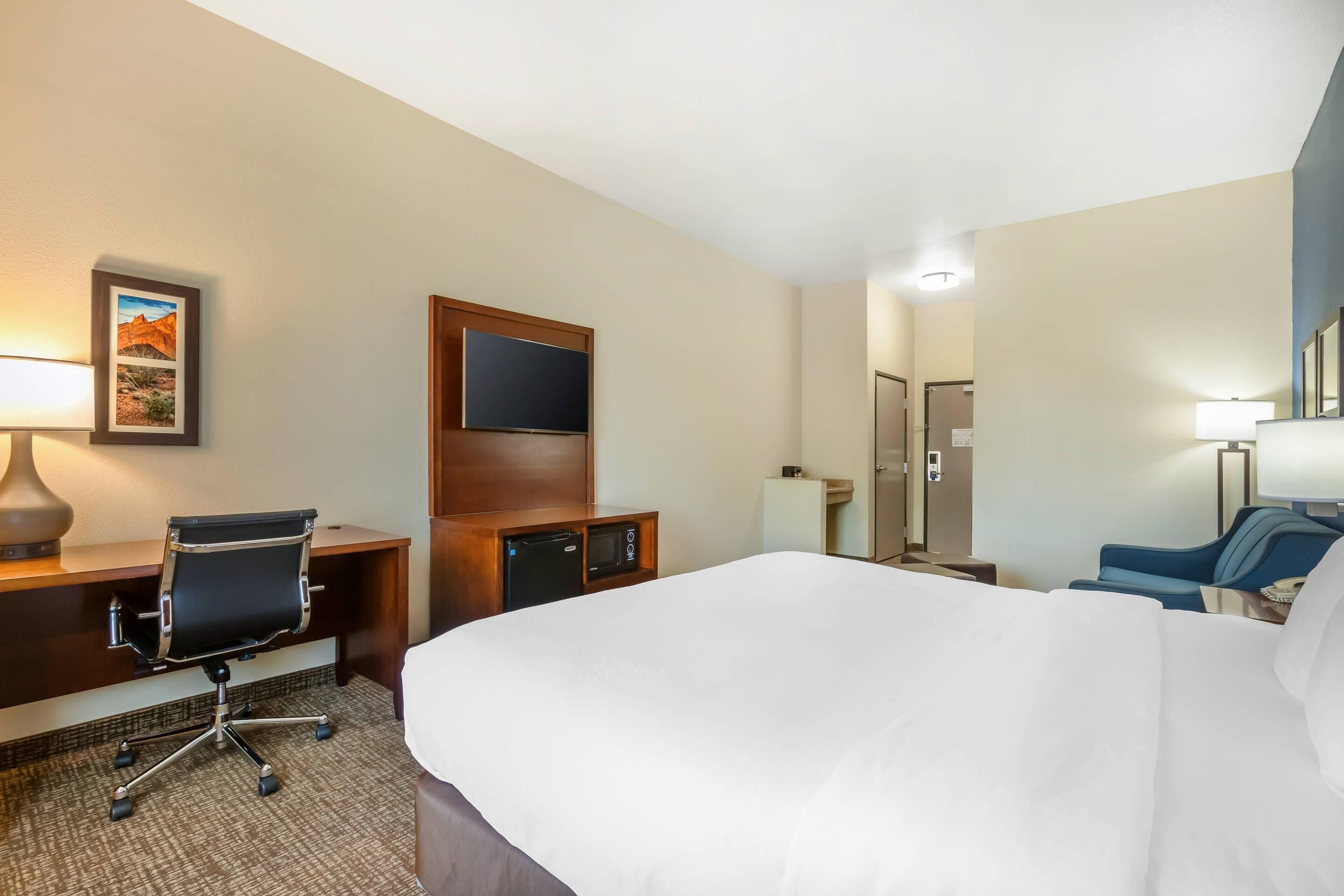 A hotel room with a bed, desk, chair, TV, and a shower area.