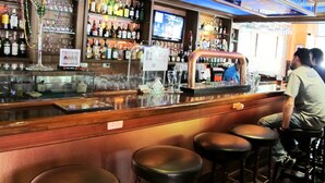 A bar area with stools, a television screen, and shelves stocked with bottles.