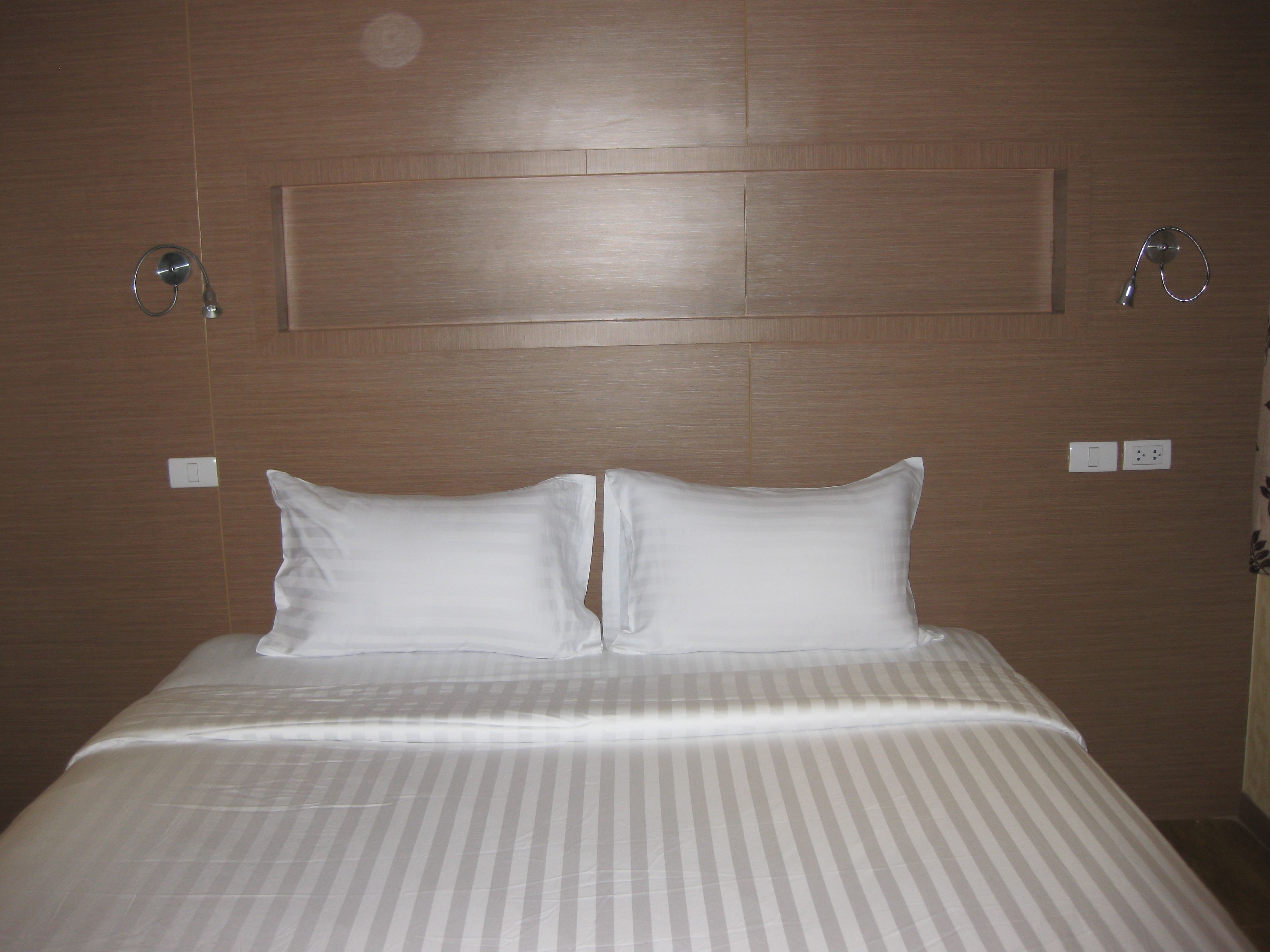 A hotel room with a large bed, a wooden headboard, and two bedside lamps.