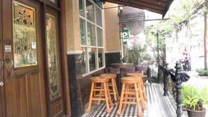 A restaurant with a green Carlsberg sign, a Heineken sign, and a Bourbon St sign. There are wooden stools and a table outside.