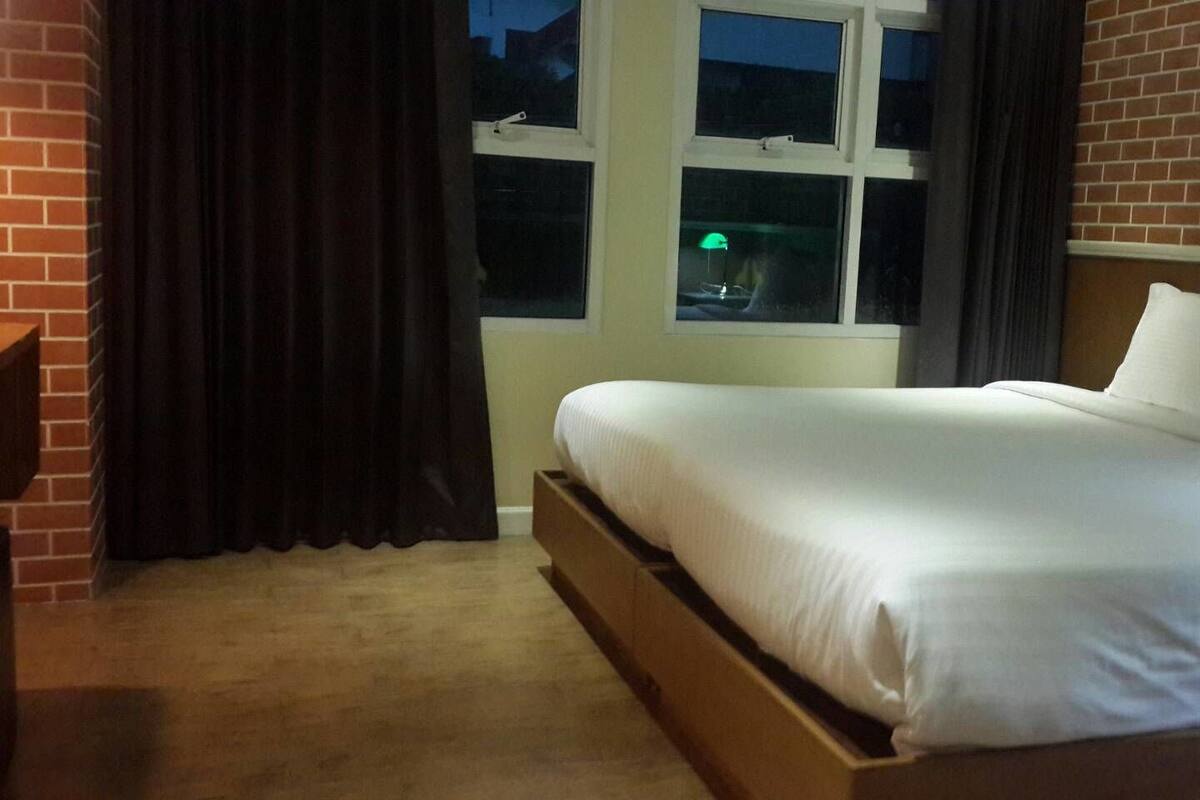 A hotel room with a single bed, a window with curtains, and a brick wall.