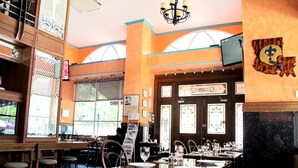 A restaurant interior with high ceilings, large windows, and a chandelier. Tables are set with plates and glasses.