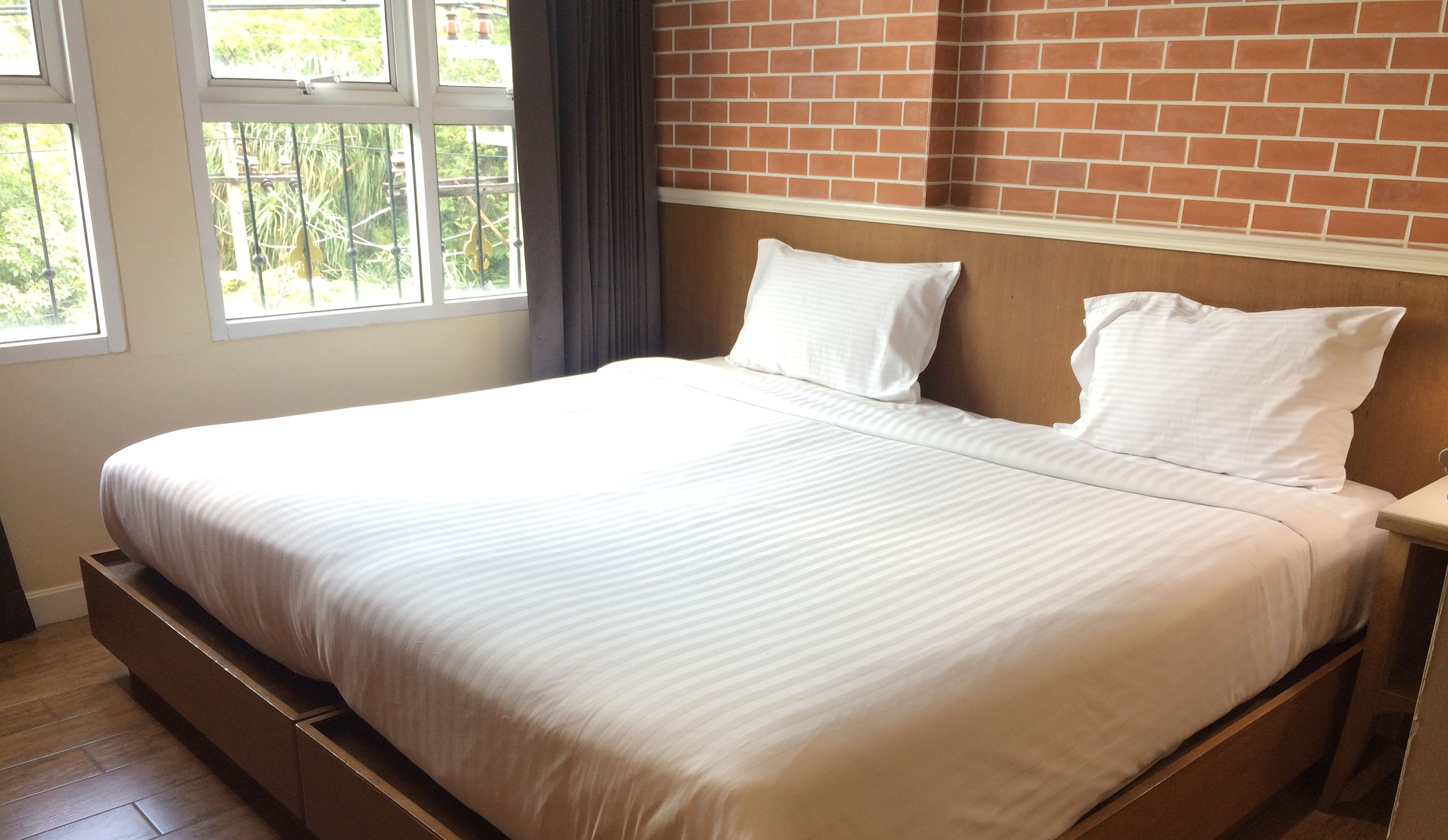 Una cama bien hecha con sábanas blancas en una habitación con pared de ladrillo y una ventana.