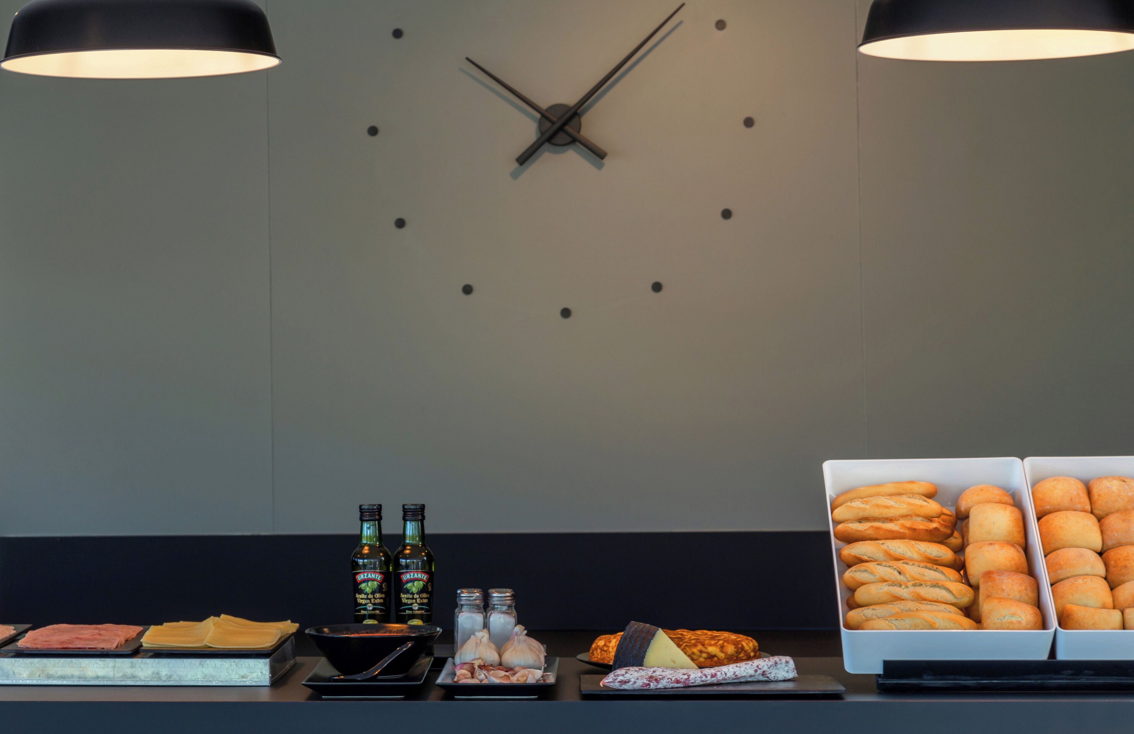 A buffet setup with various food items, including meats, cheeses, and breads, and a clock on the wall.