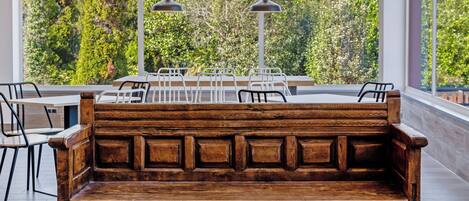 A wooden bench with intricate carvings in a modern room with large windows and metal chairs.