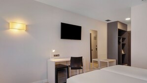 Et moderne hotelværelse med seng, skrivebord med computer, tv og garderobeskab.