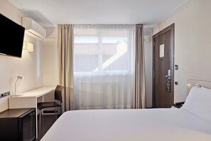A hotel room with a bed, a desk, a chair, a TV, and a window with curtains. - B&B Hotel Oviedo (Siero)