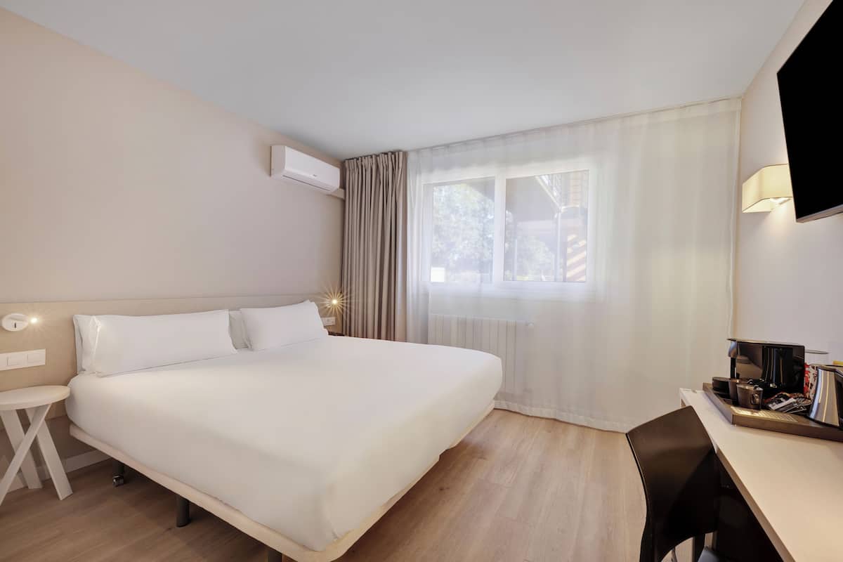 Habitación de hotel con una cama grande, un escritorio, una silla, un televisor y una ventana con cortinas.