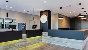Et moderne hotelområde med reception, digital check-in kiosk og en logo på væggen.