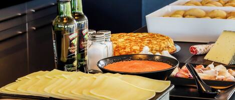Une table de buffet proposant divers aliments, notamment du fromage, du jambon et un plat avec une sauce rouge. On y trouve également des bouteilles de vin, ainsi que des salières et des poivrières.