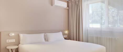 A modern hotel room with a large bed, a bedside table, an air conditioning unit, and a window with curtains.
