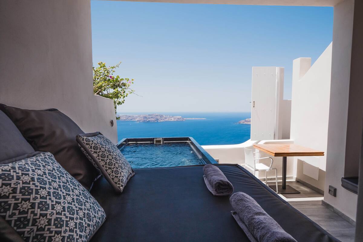 A bedroom with a view of the sea, a bathtub, and a table.