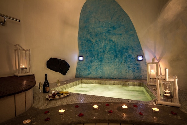 A spa area with a hot tub, candles, and rose petals on the floor. - Galaxy Suites & Villas (Santorini)