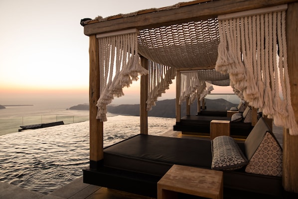 Terraza de madera con vista al mar al atardecer, que incluye una zona de estar con cojines y una pequeña mesa.