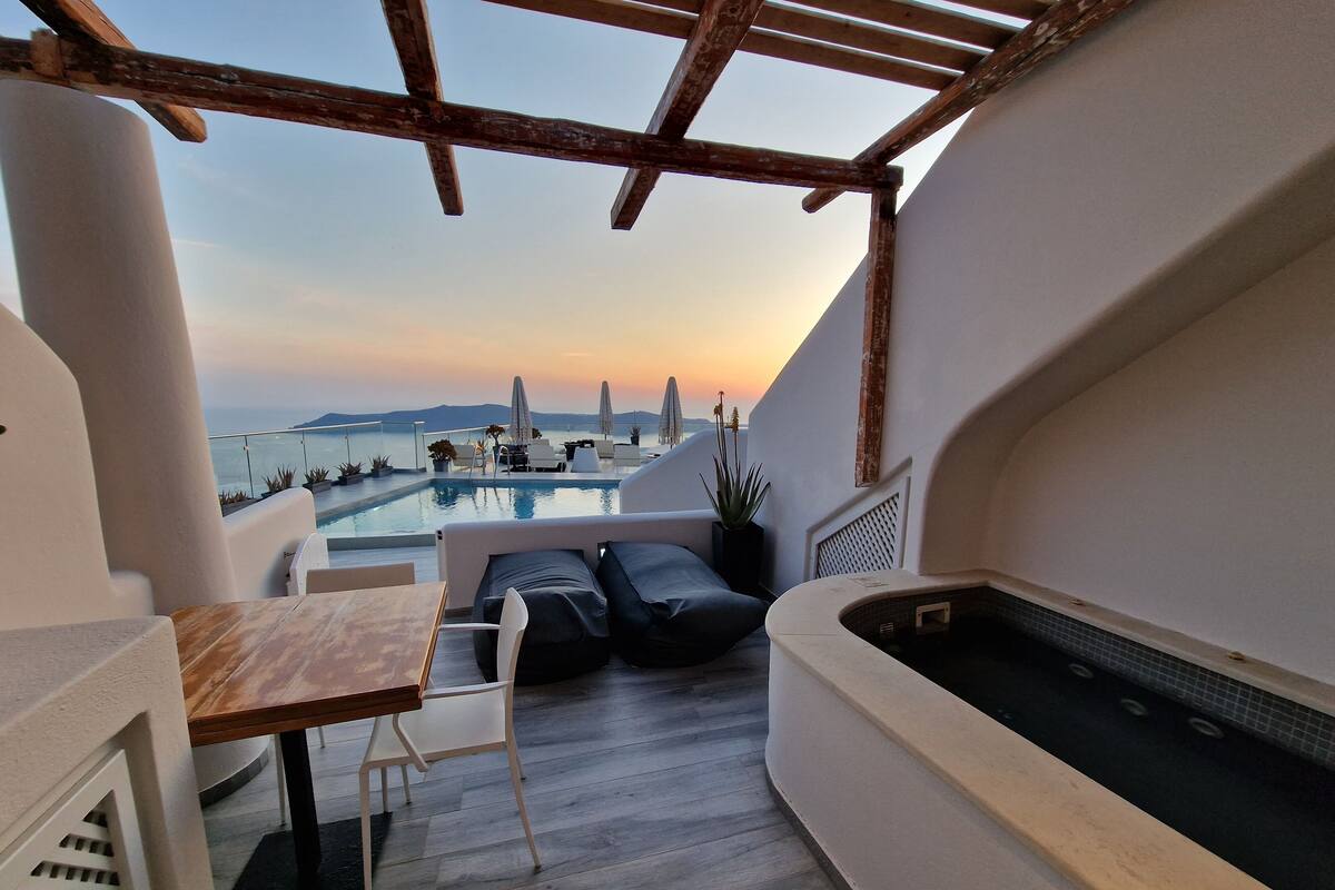 A rooftop terrace with a pool, seating area, and a view of the sea at sunset.