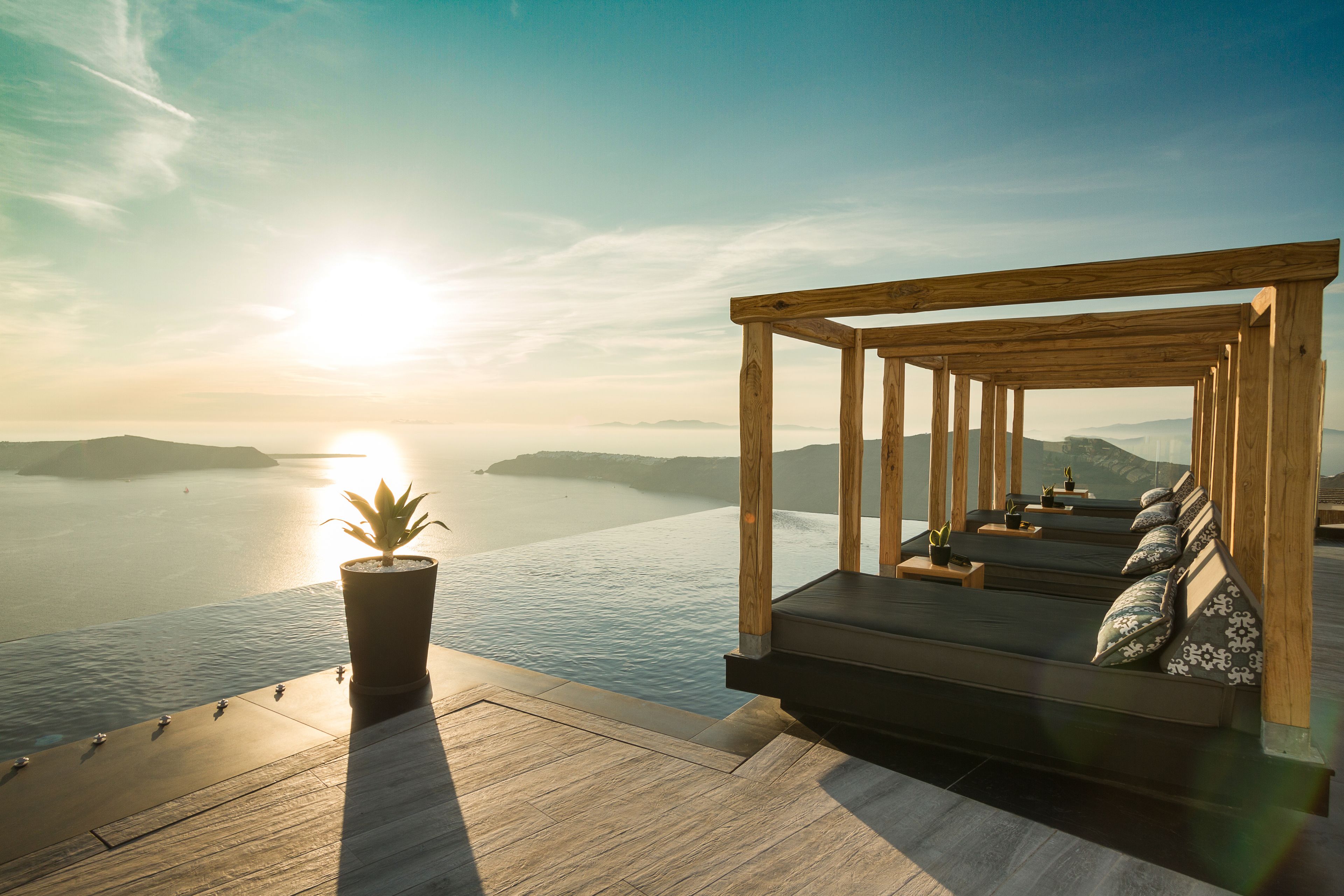 A wooden deck with a built-in seating area overlooking a body of water, a potted plant, and a clear sky.