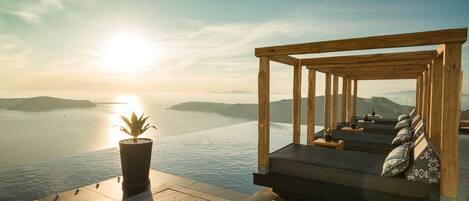 A wooden deck with a built-in seating area overlooking a body of water, a potted plant, and a clear sky.