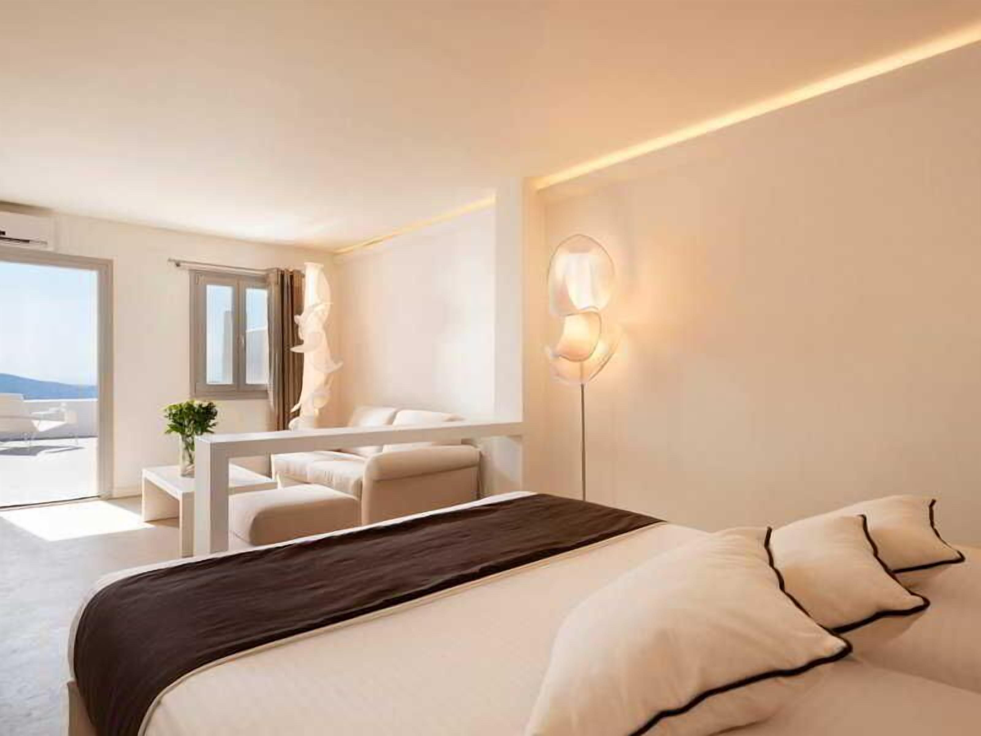 A modern hotel room with a bed, a desk, a chair, a lamp, and a view of the outdoors.
