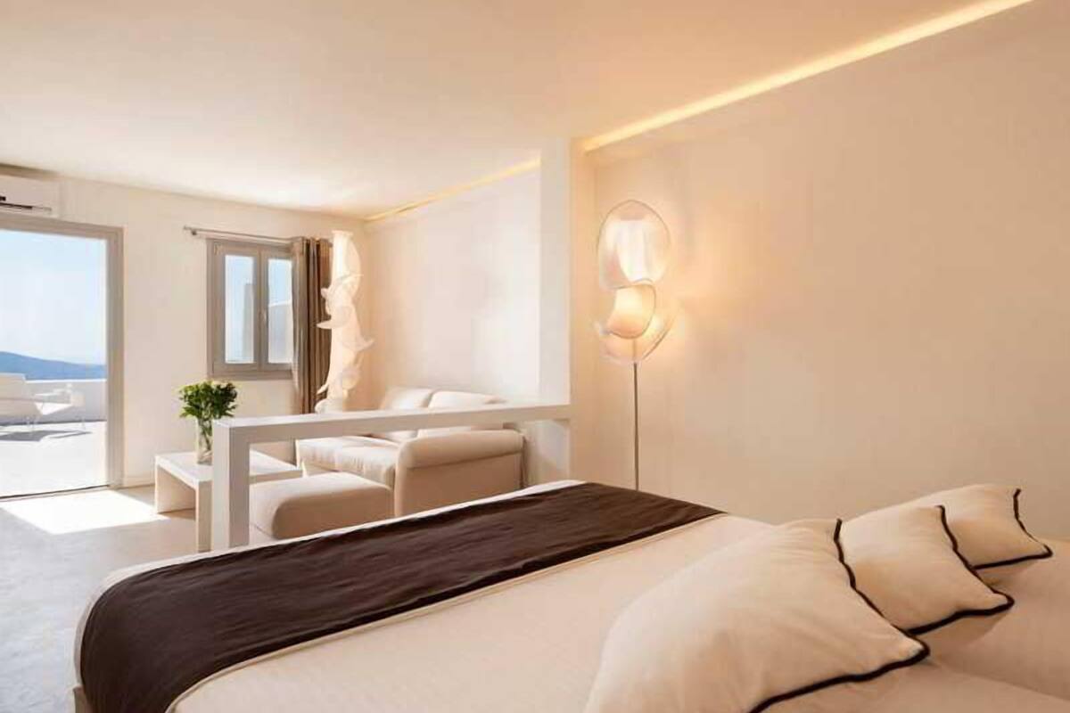 A modern hotel room with a bed, a bedside table, a lamp, and a view of the outdoors.