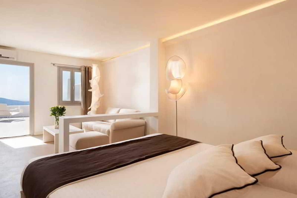 Ein modernes Hotelzimmer mit Bett, Schreibtisch, Stuhl, Lampe und Blick ins Freie.