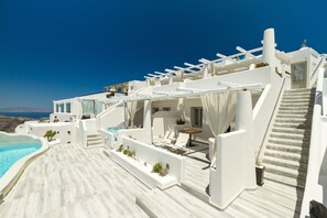 A white building with a pool, outdoor seating, and a staircase leading to a terrace. - Galaxy Suites & Villas (Santorini)
