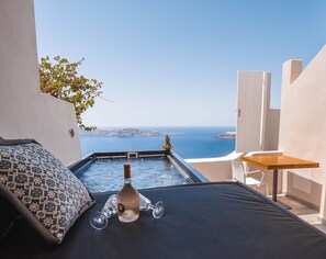 A balcony with a bed, a hot tub, and a wooden table. - Galaxy Suites & Villas (Santorini)