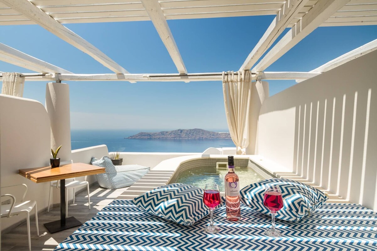 Un balcón con vistas al mar, una mesa con una botella de licor y una silla.