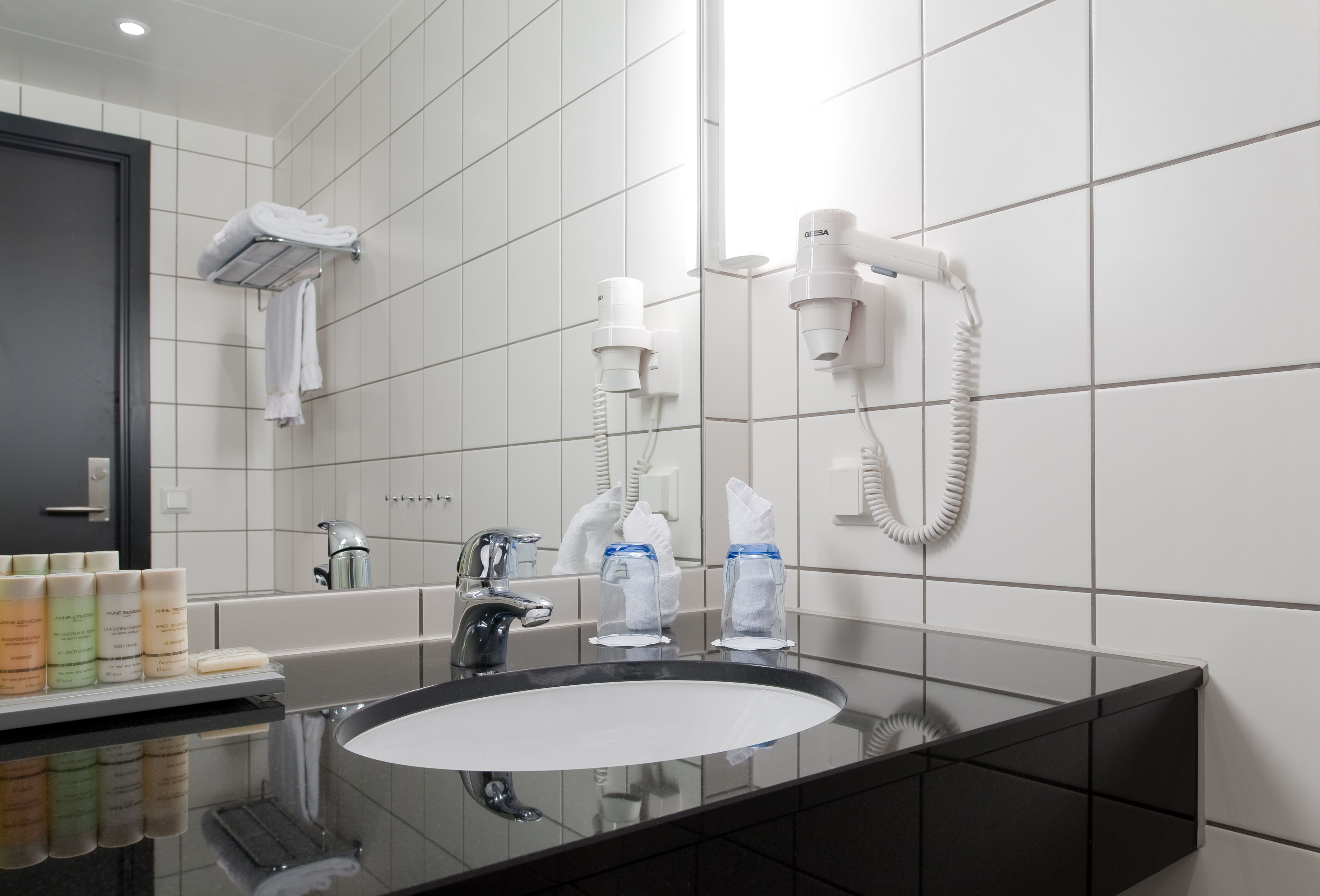 A modern bathroom with a large mirror, a black sink, and two hair dryers mounted on the wall.