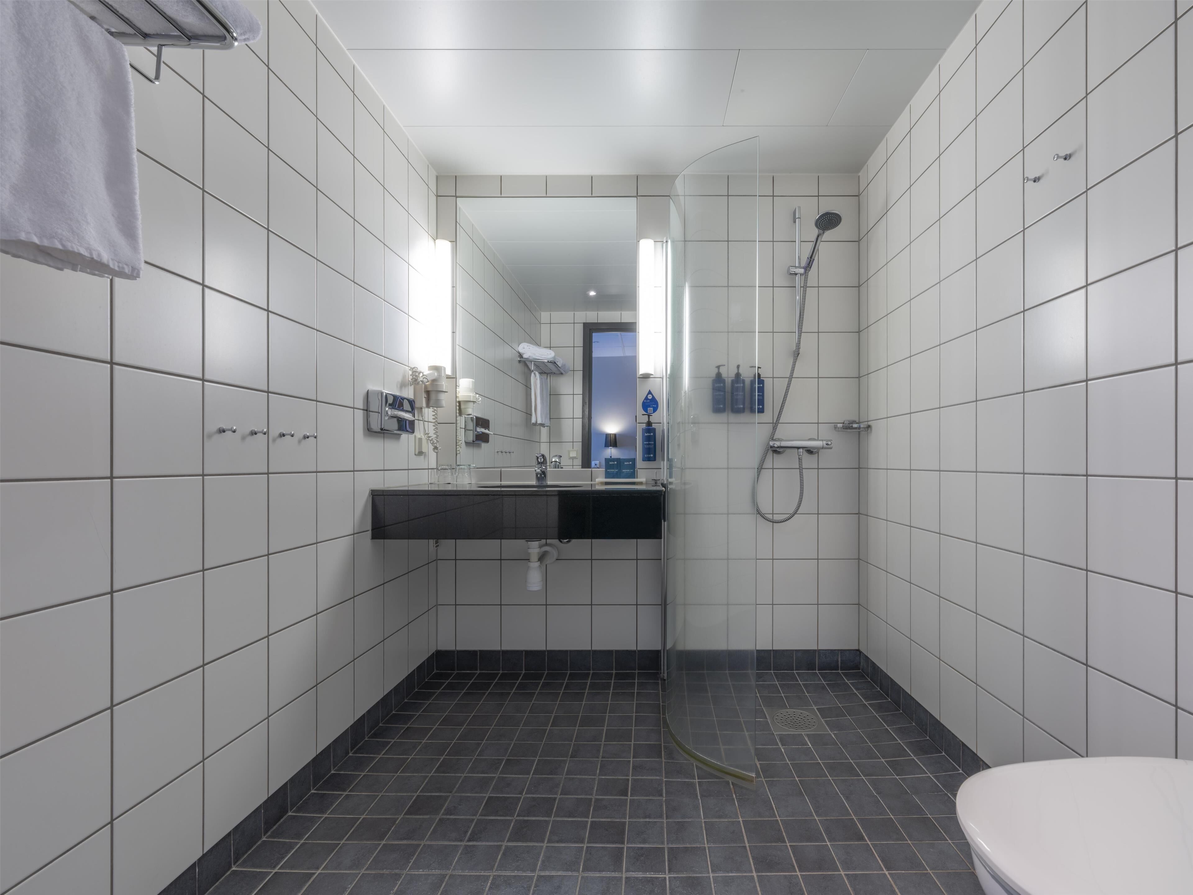 Un baño moderno con azulejos blancos, un lavamanos negro, una cabina de ducha de cristal y un inodoro.
