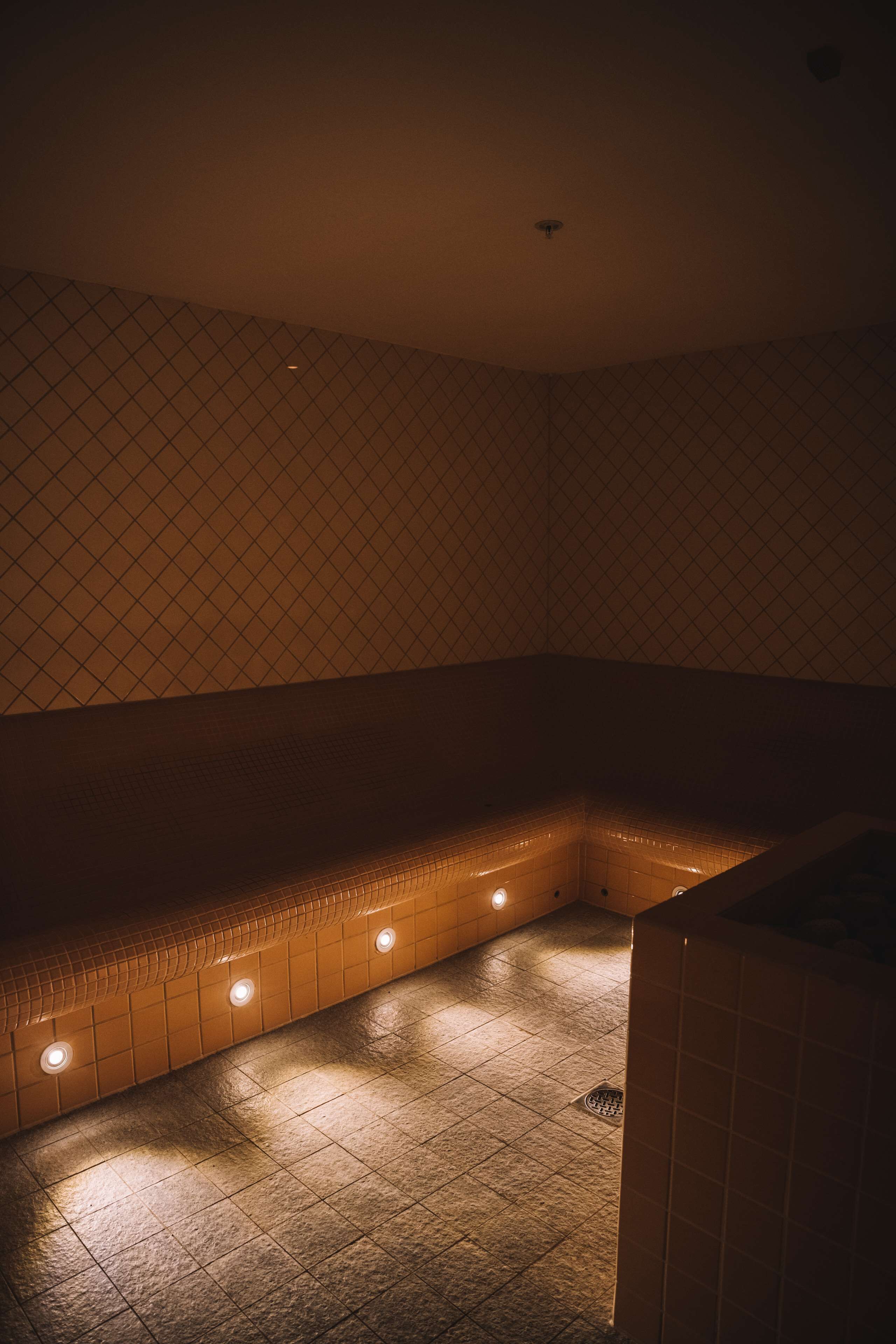 Una habitación con poca luz, suelo de baldosas y un banco a lo largo de la pared.