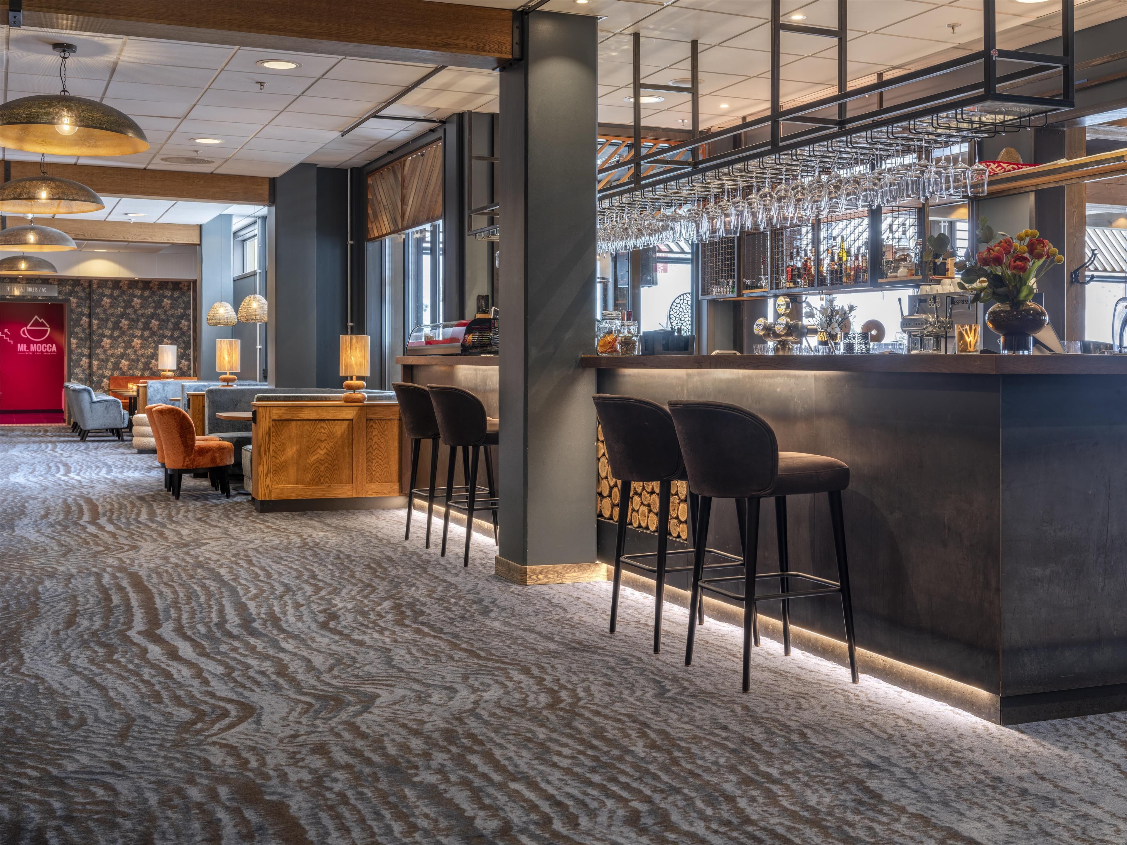 A modern bar area with a bar counter, multiple stools, and hanging wine glasses.