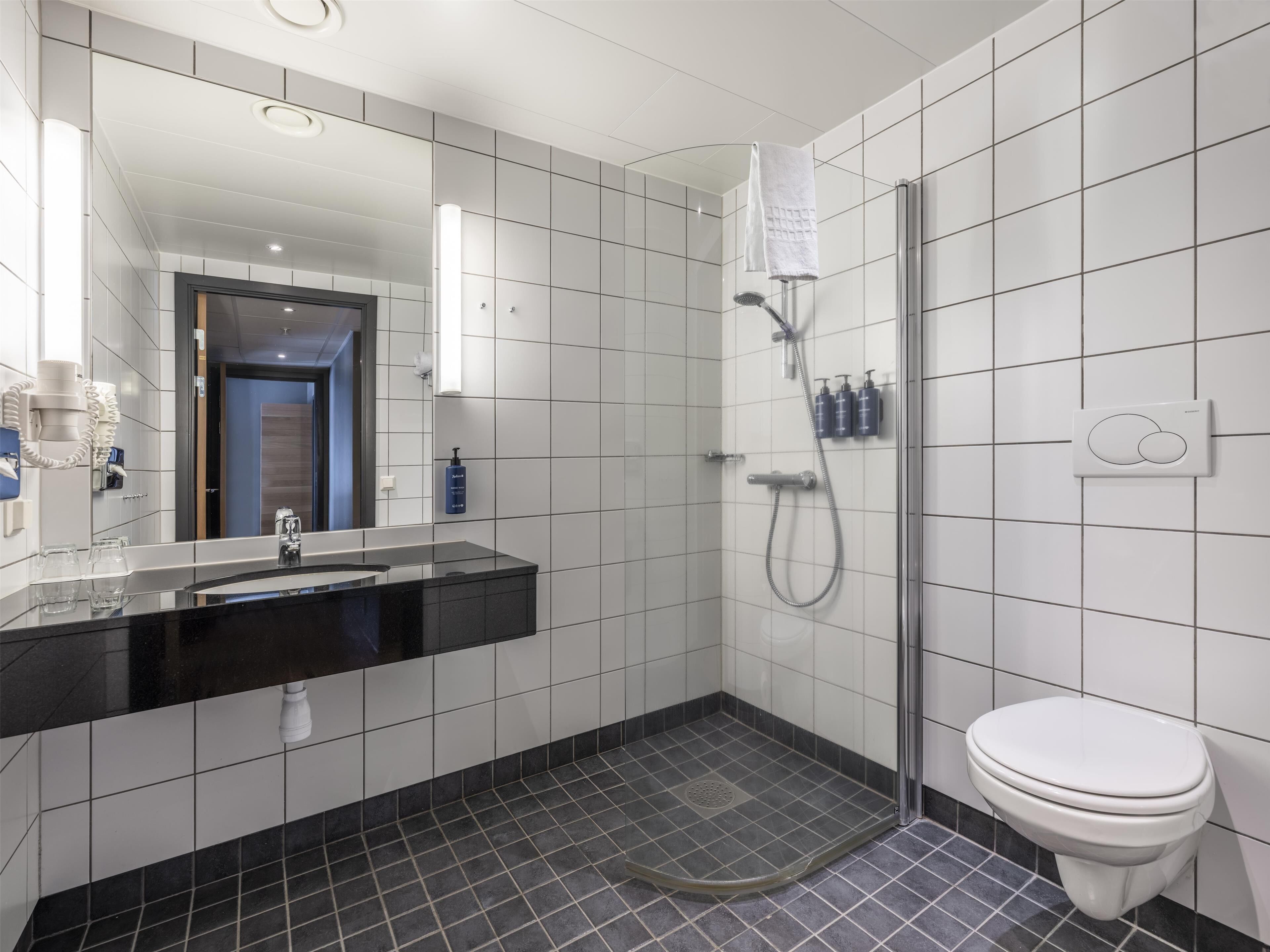 Uma casa de banho moderna com lavatório preto, azulejos brancos, cabine de duche em vidro e sanita branca.