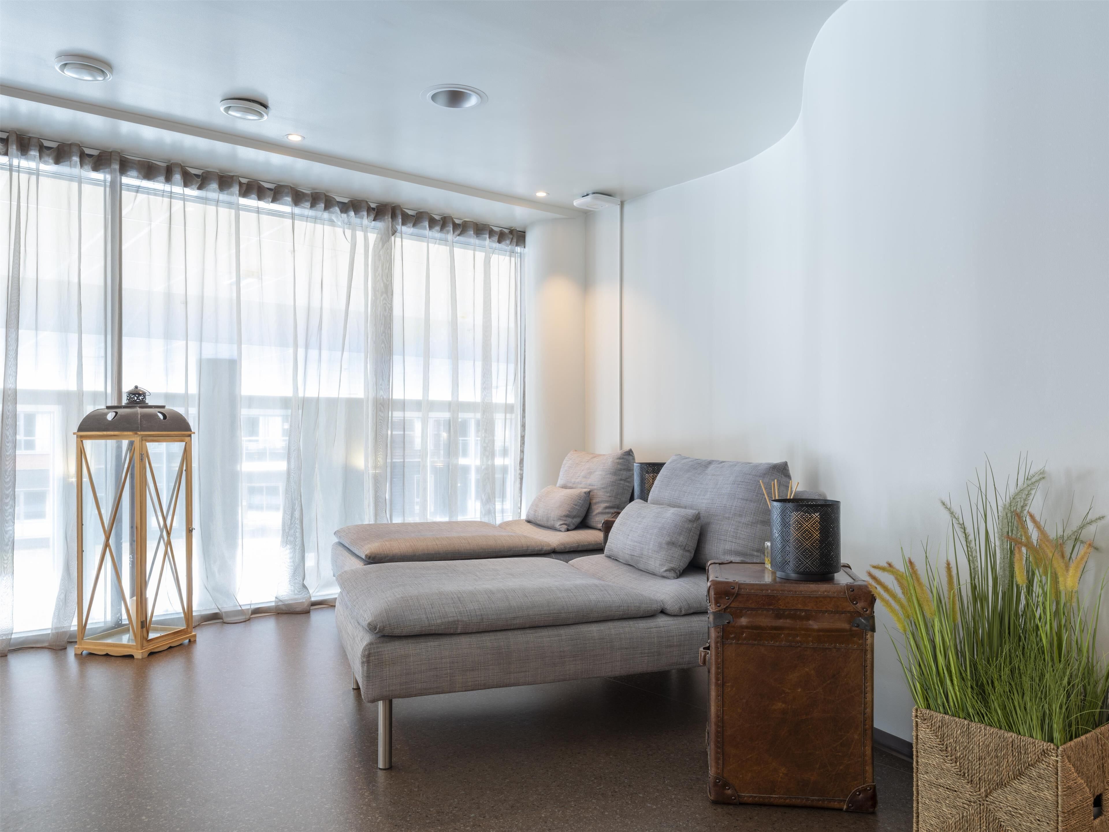 A modern bedroom with a sofa bed, a wooden side table, and a potted plant.
