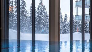 Piscina interior com paredes de vidro transparente que refletem a paisagem nevada lá fora.