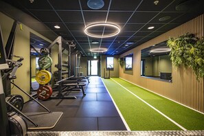 A gym with weightlifting equipment, a green artificial turf area, and a wall-mounted plant.
